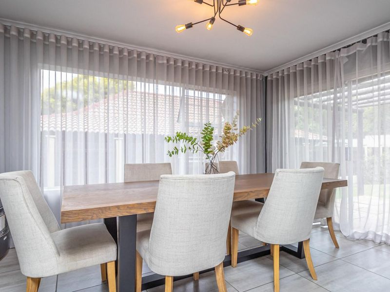 A bright and modern dining area featuring large windows with floor-to-ceiling sheer curtains, tiled flooring, and a contemporary overhead light fixture.