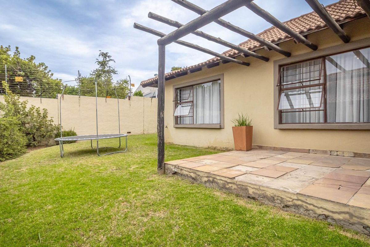 Rear exterior view featuring a paved patio area with a timber pergola, overlooking a private garden enclosed by boundary walls with electric fencing.