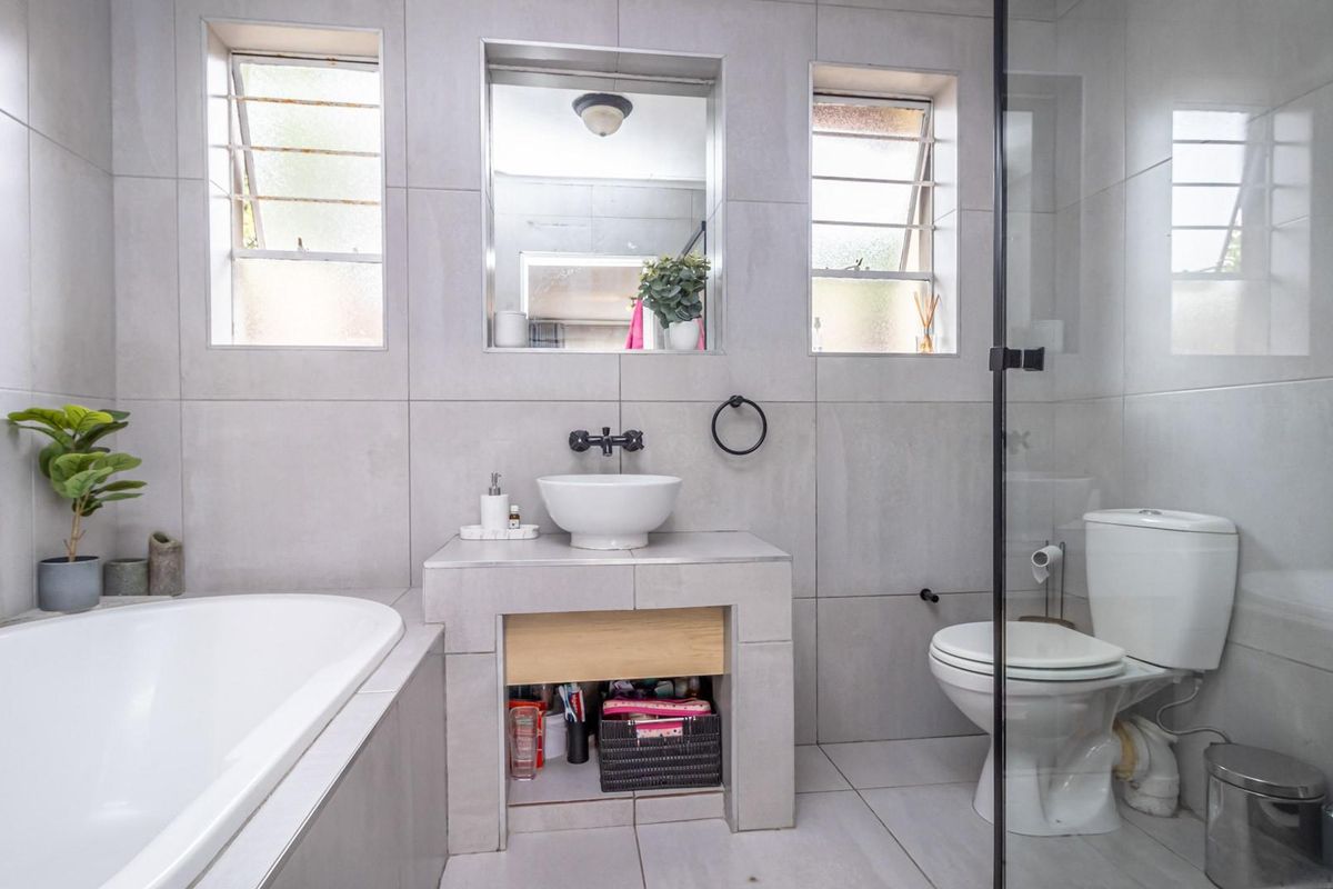 Modern bathroom featuring a built-in bathtub, glass-enclosed shower, vessel sink vanity, and neutral floor-to-ceiling tiling.