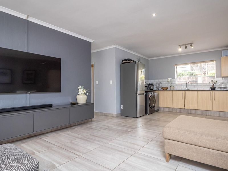 An open-plan living and kitchen area featuring modern grey cabinetry, light wood kitchen cupboards, subway tile backsplash, and neutral tiled flooring throughout.
