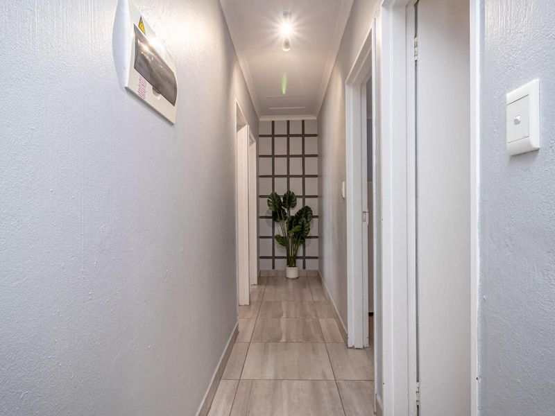 A clean, well-lit hallway featuring neutral tiled flooring and access to multiple rooms, providing a functional transition space within the home.