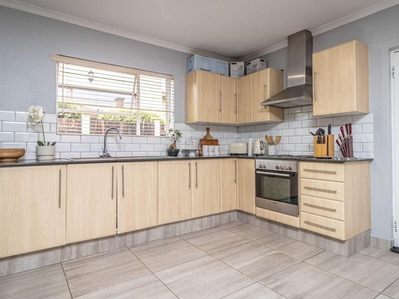 A functional kitchen featuring light wood cabinetry, subway tile backsplash, stainless steel oven and extractor fan, and tiled flooring.