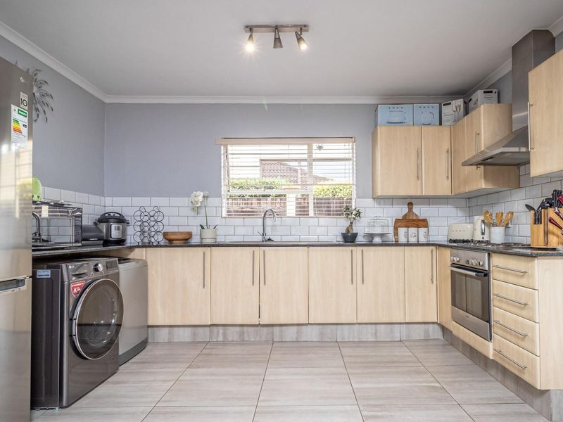 A functional kitchen featuring light wood cabinetry, subway tile backsplash, stainless steel appliances, and tiled flooring with integrated laundry space.
