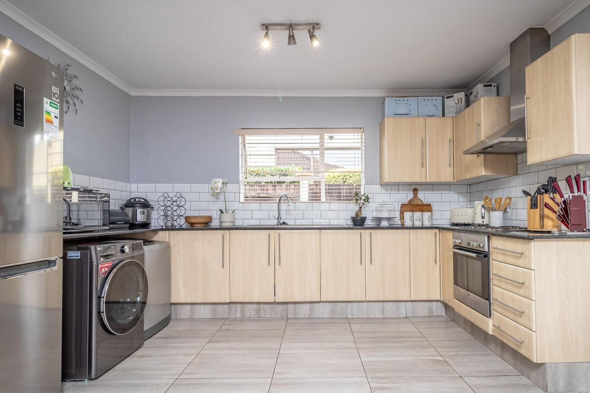 A functional kitchen featuring light wood cabinetry, subway tile backsplash, stainless steel appliances, and tiled flooring with integrated laundry space.