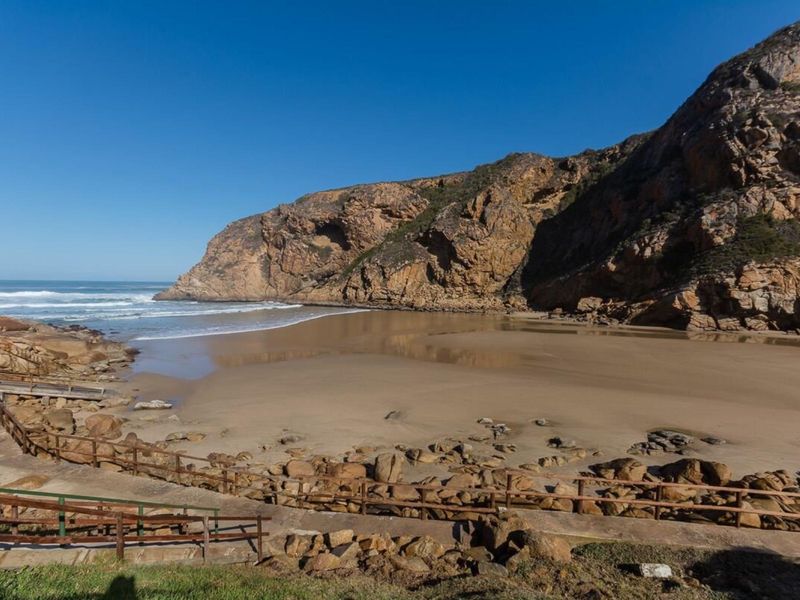 A scenic view of a coastal beach area featuring a wooden boardwalk and natural rock formations along the shoreline.