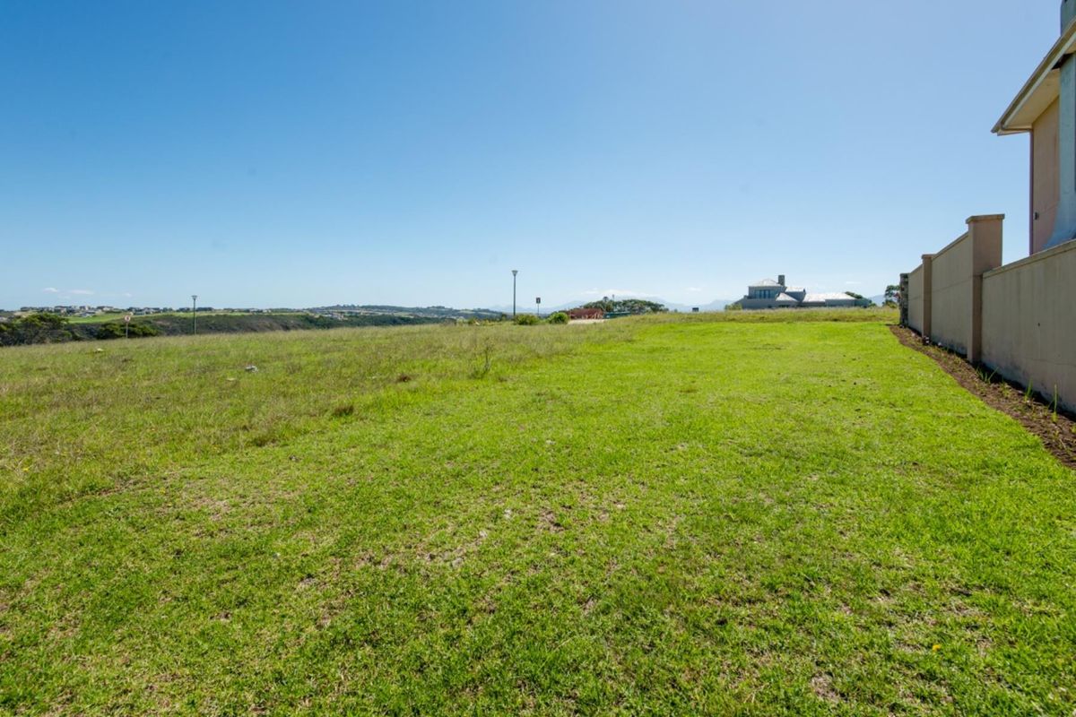 A spacious, well-maintained vacant residential plot featuring a level lawn and a solid boundary wall, offering open views of the surrounding landscape.