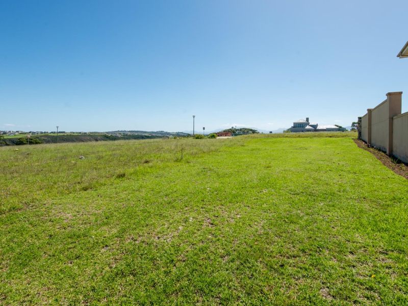 A spacious, well-maintained vacant residential plot featuring a level lawn and a solid boundary wall, offering open views of the surrounding landscape.