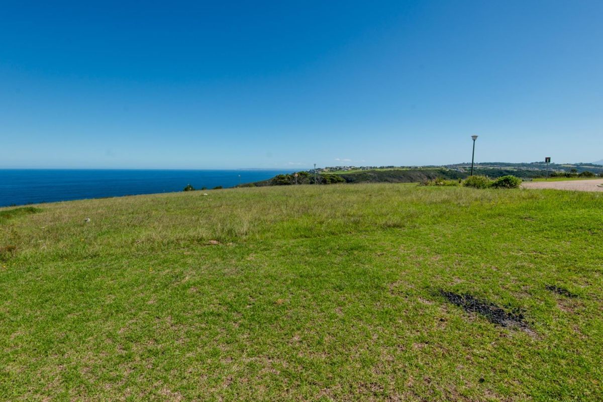 A scenic view of the coastline and ocean from a vacant residential plot, featuring clear horizon lines and natural grass landscape.