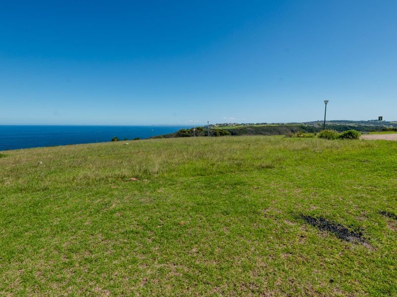 A scenic view of the coastline and ocean from a vacant residential plot, featuring clear horizon lines and natural grass landscape.