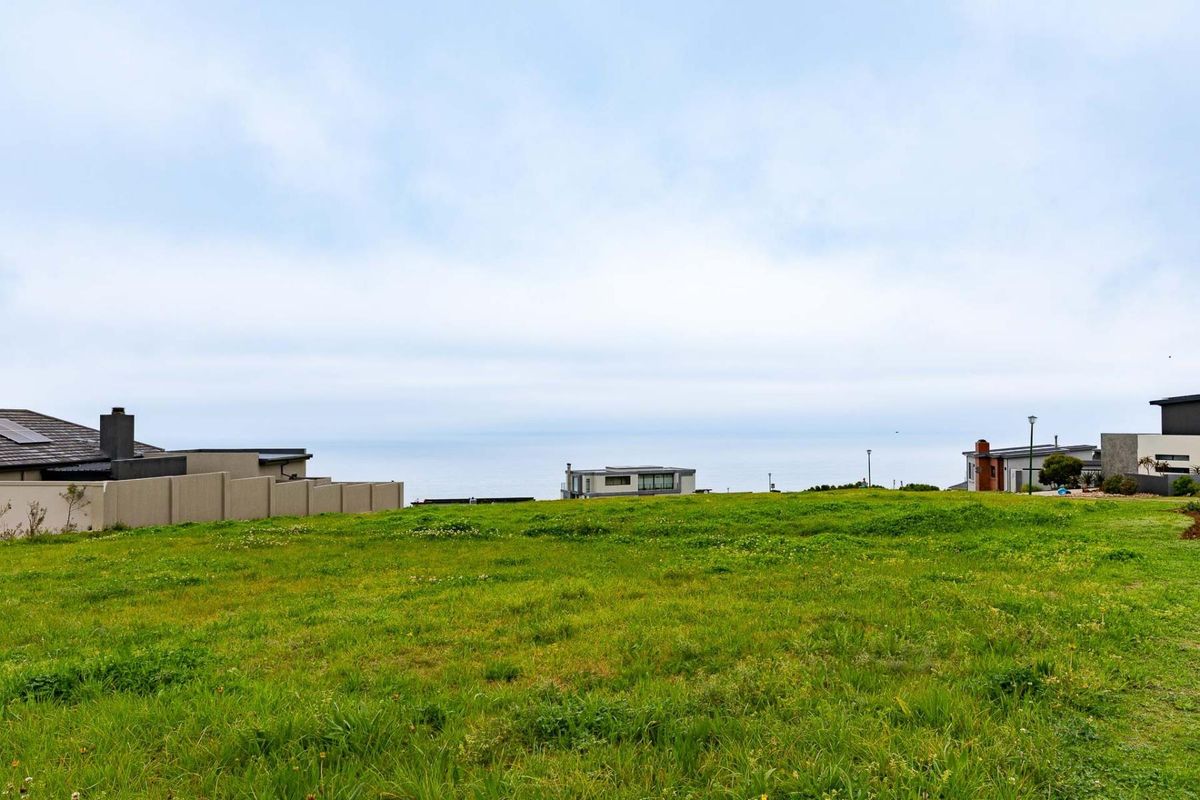 A vacant residential plot featuring expansive green space with a clear view of the coastal horizon and surrounding neighborhood.