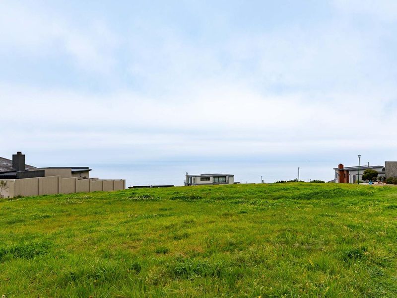 A vacant residential plot featuring expansive green space with a clear view of the coastal horizon and surrounding neighborhood.