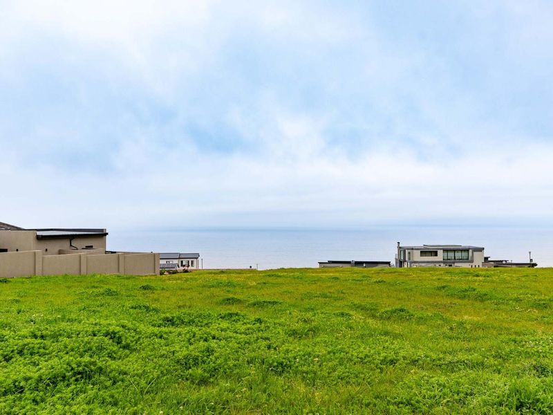 A scenic view of the ocean from a vacant residential plot, showcasing the coastal landscape and surrounding neighborhood.