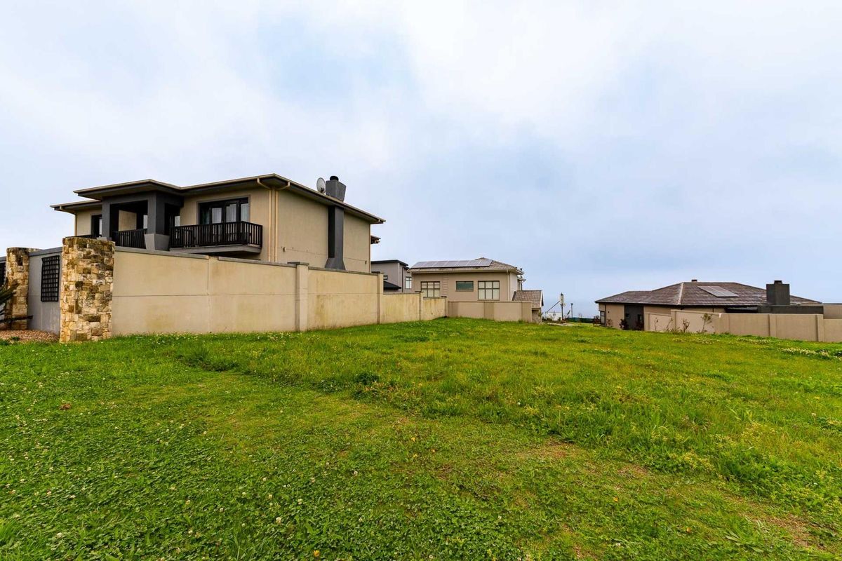 A vacant residential plot featuring a well-maintained grass lawn, enclosed by a boundary wall with stone cladding accents, adjacent to established residential properties.