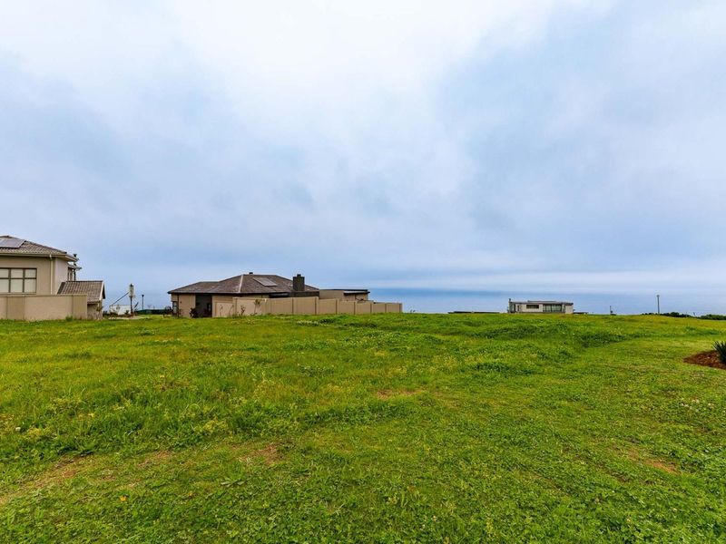 A vacant residential plot featuring open grassland with surrounding boundary walls and distant ocean views.