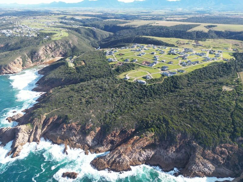 An aerial view of a coastal residential estate situated on a cliffside, showcasing the surrounding landscape and ocean proximity.