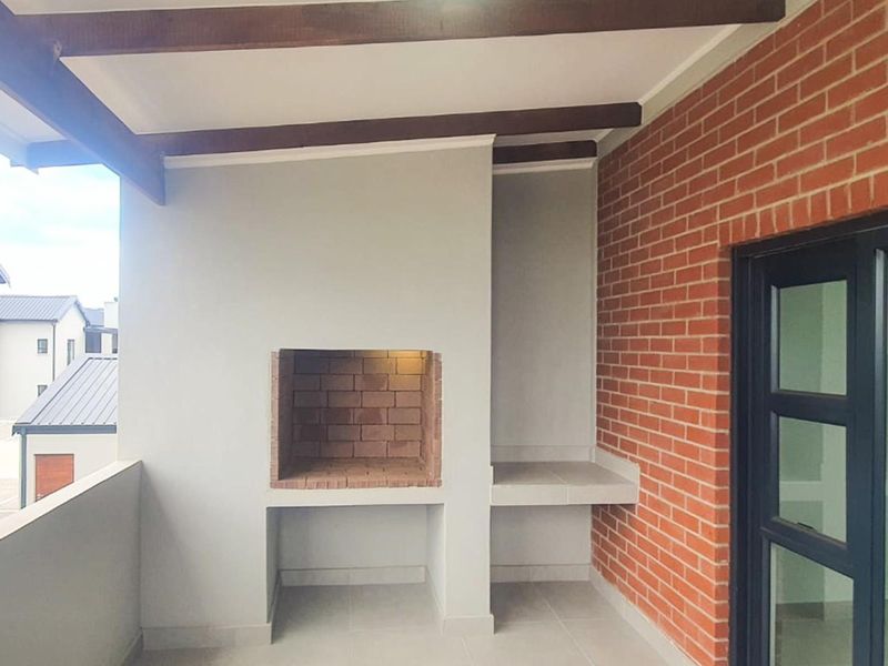 Covered balcony featuring a built-in brick braai, exposed timber ceiling beams, and a feature brick wall, providing an ideal space for outdoor entertaining.