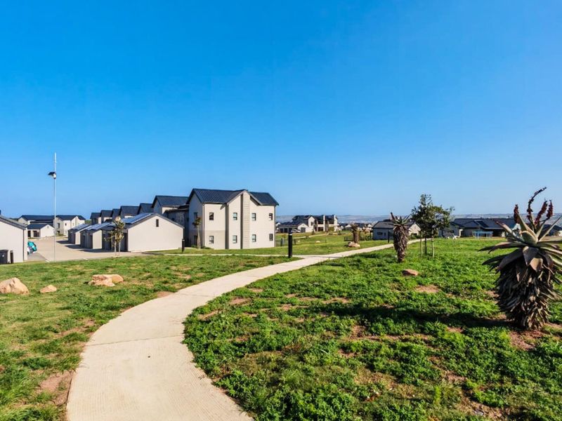 A view of the residential complex featuring a concrete pathway winding through a landscaped lawn with modern apartment buildings in the background.