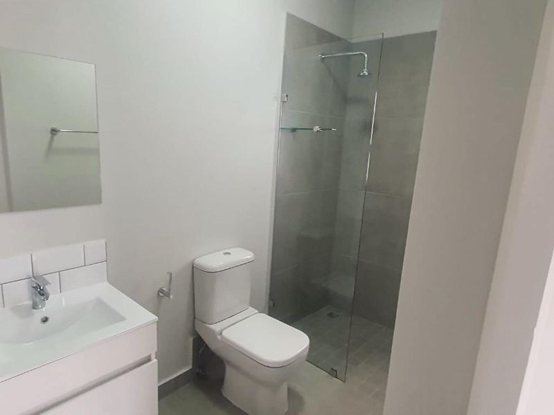 Modern bathroom featuring a vanity cabinet with basin, a toilet, and a walk-in shower with a glass screen and tiled surround.