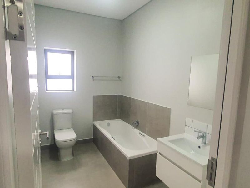 A clean, modern bathroom featuring a bathtub, a wall-mounted vanity with a basin, and neutral floor and wall tiling.