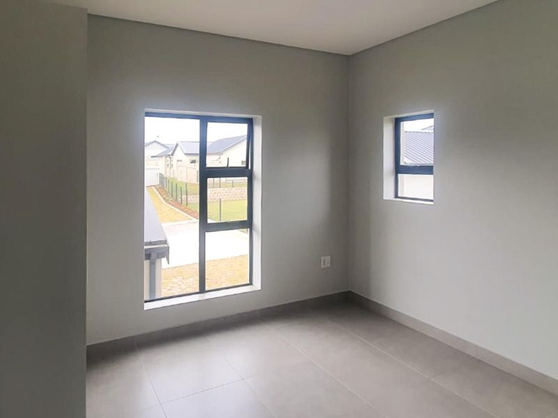 A bright, empty bedroom featuring neutral tiled flooring, modern aluminium window frames, and clean, freshly painted walls.