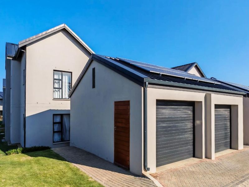 Modern apartment exterior featuring a double garage with automated doors, solar panels on the roof, and a neat paved driveway.