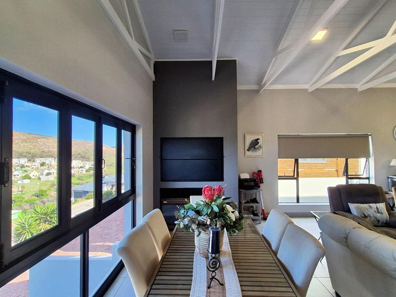 Spacious open-plan living and dining area featuring a vaulted ceiling with exposed trusses, a built-in fireplace, and large windows offering scenic views.