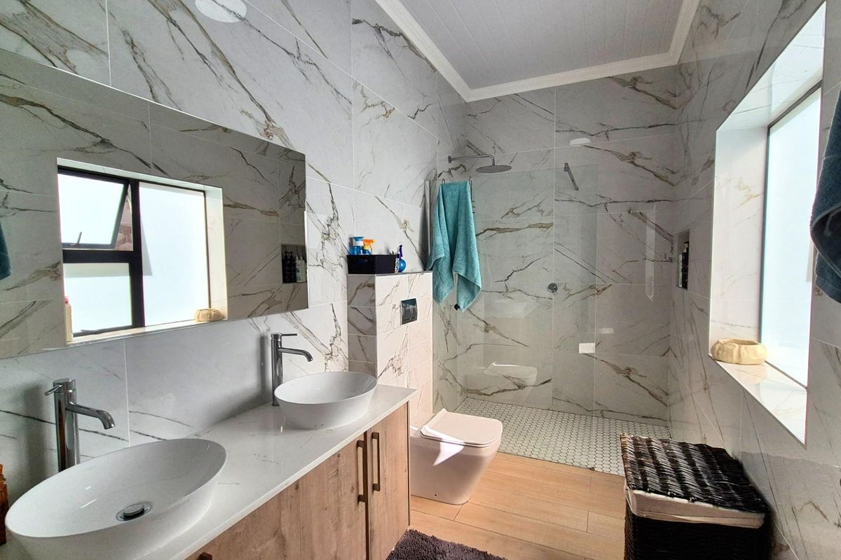 Modern bathroom featuring a double vanity with vessel sinks, wall-mounted faucets, a walk-in shower with glass screen, and elegant marble-look wall tiling.