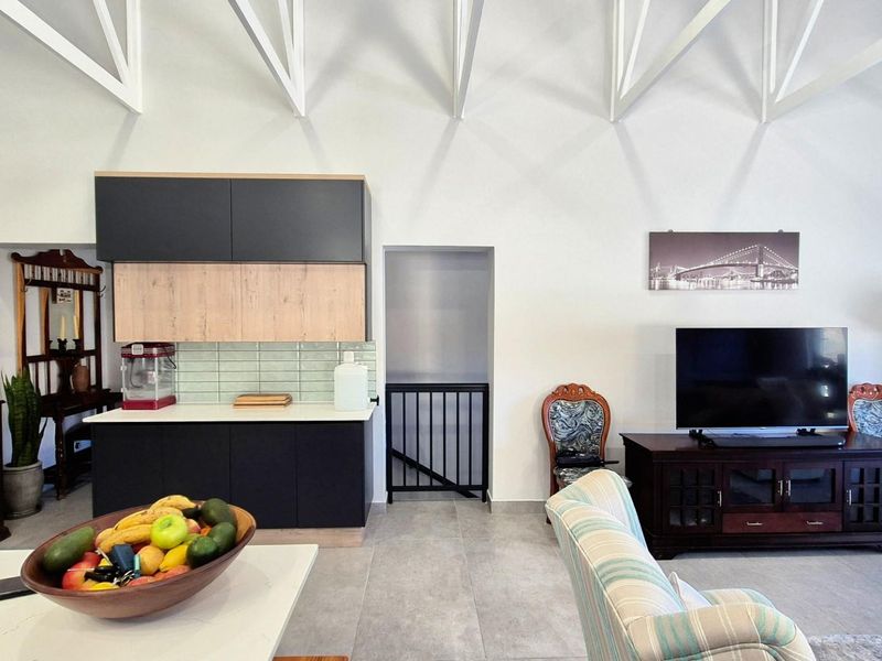 Open plan living area featuring high ceilings with exposed trusses, modern two-tone kitchen cabinetry, and neutral tiled flooring.