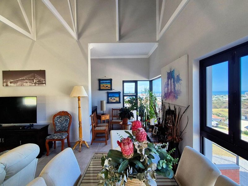 Spacious open-plan living area featuring high vaulted ceilings with exposed trusses, large windows, and scenic coastal views.