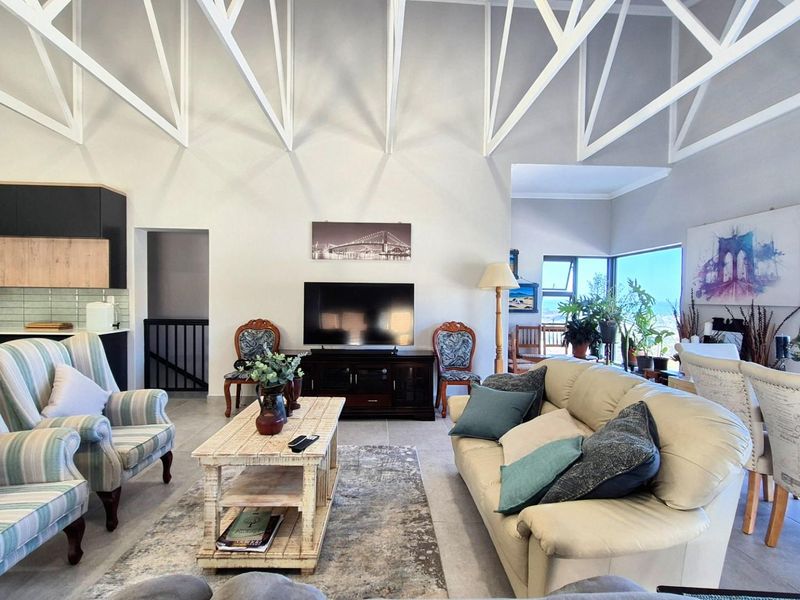 Spacious open-plan living area featuring high vaulted ceilings with exposed white trusses, tiled floors, and an integrated kitchen with modern cabinetry.