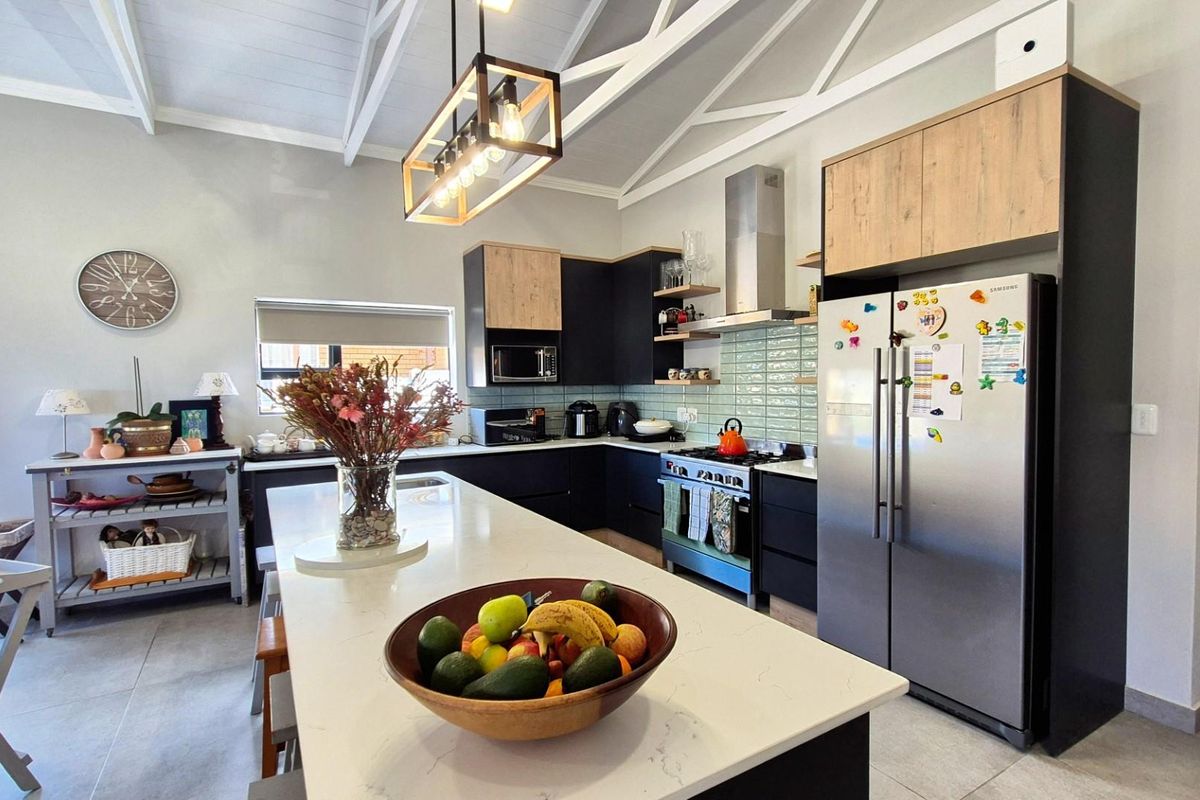 Modern kitchen featuring a large central island with quartz countertops, sleek two-tone cabinetry, subway tile backsplash, and vaulted ceilings with exposed trusses.