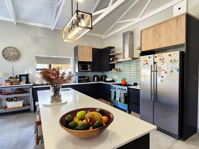 Modern kitchen featuring a large central island with quartz countertops, sleek two-tone cabinetry, subway tile backsplash, and vaulted ceilings with exposed trusses.