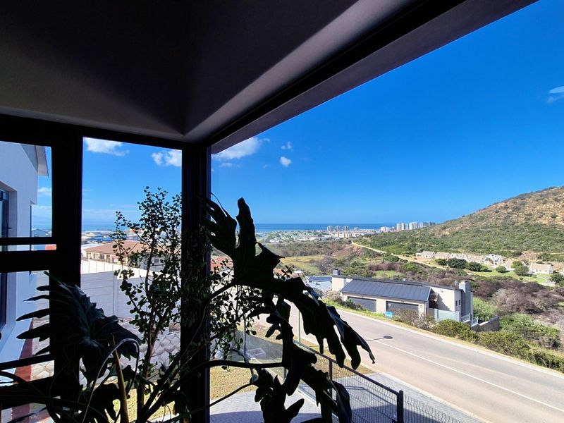 A scenic elevated view overlooking the surrounding landscape, coastal area, and neighbourhood, framed by large modern windows.