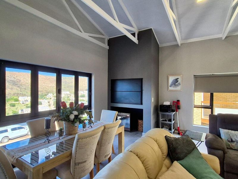 Spacious open-plan living and dining area featuring a vaulted ceiling with exposed trusses, a built-in fireplace, and large windows offering scenic views.