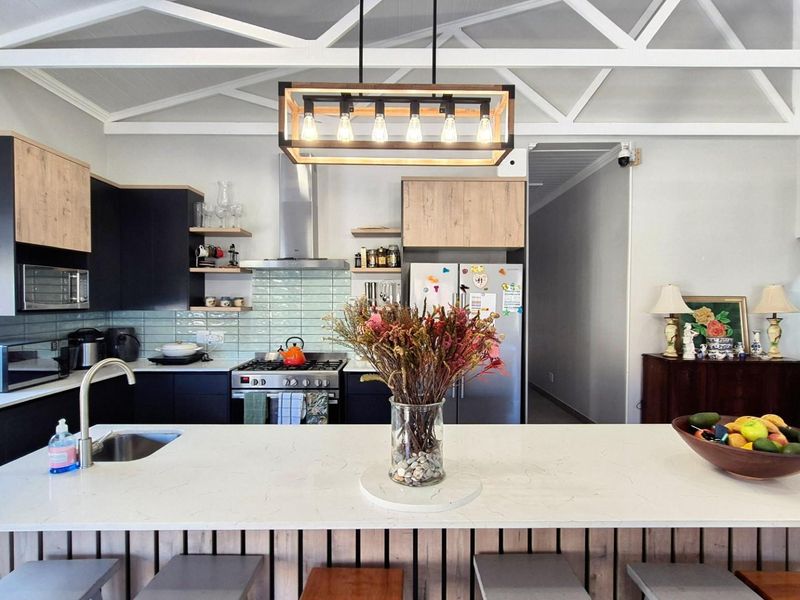 Modern kitchen featuring a large central island with quartz countertops, sleek cabinetry, subway tile backsplash, and exposed white roof trusses.