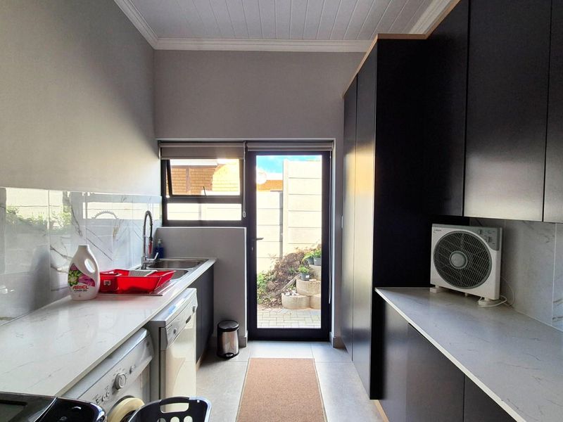 Modern scullery featuring sleek dark cabinetry, stone countertops, marble-look splashbacks, and direct access to the exterior.