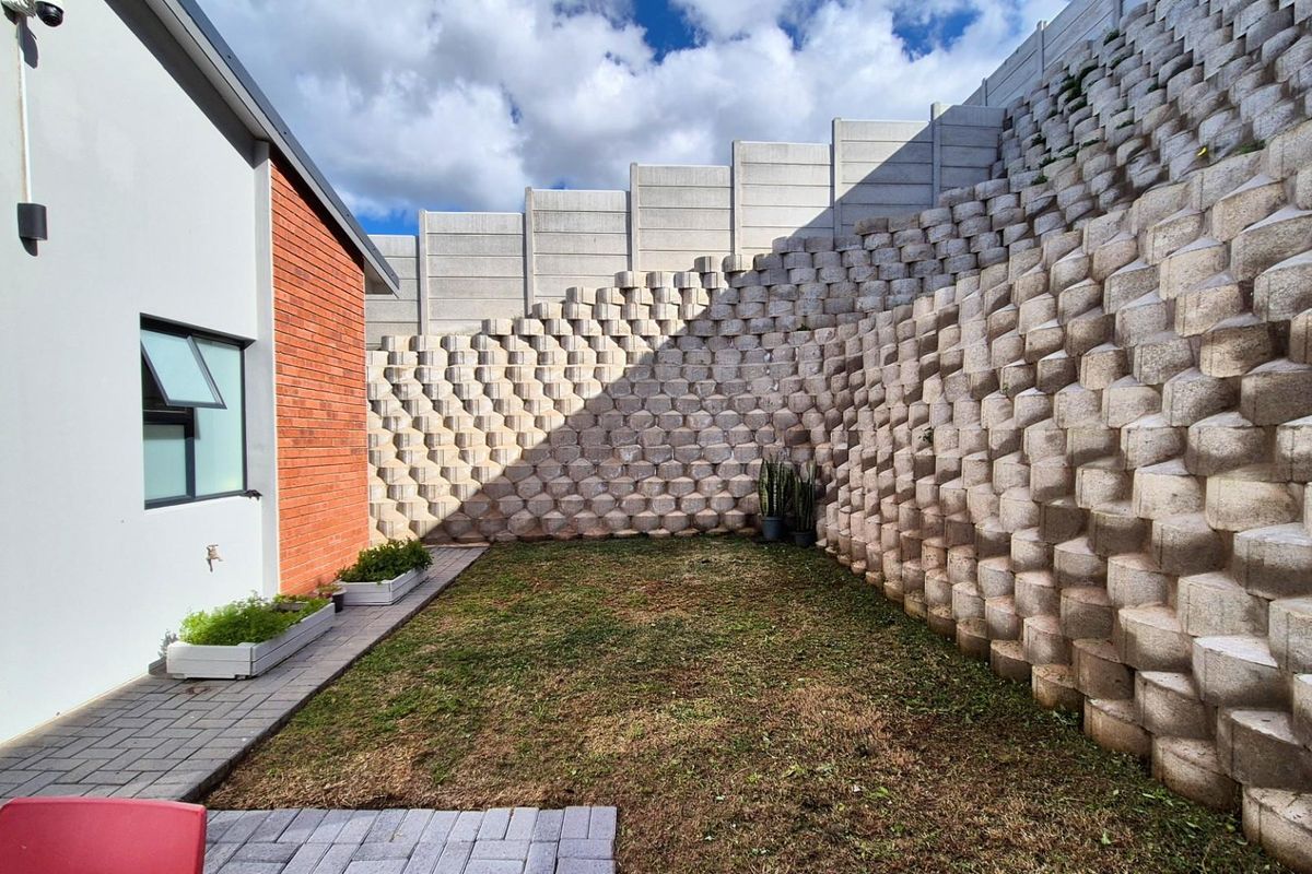 A private rear garden area featuring a substantial tiered concrete retaining wall, paved walkway, and a combination of brick and plastered exterior wall finishes.