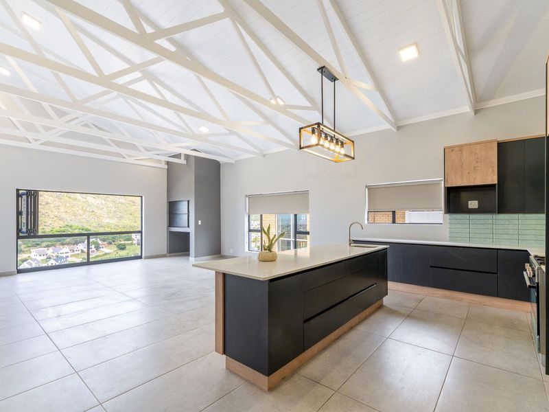 Spacious open-plan living area featuring a modern kitchen with island, high vaulted ceilings with exposed trusses, and a built-in fireplace with scenic views.