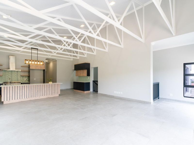 Spacious open-plan living area featuring high exposed roof trusses, modern kitchen with island, tiled flooring, and contemporary finishes throughout.