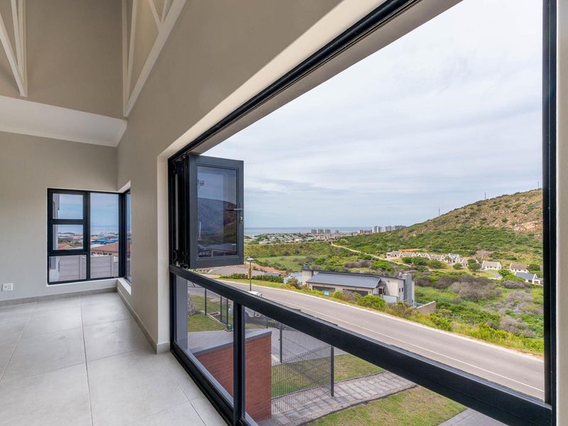 A bright, modern balcony featuring tiled floors, a glass balustrade, and expansive views of the surrounding landscape and coastline.