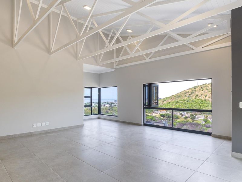 Spacious open-plan living area featuring high ceilings with exposed white trusses, large windows with scenic views, and modern tiled flooring.