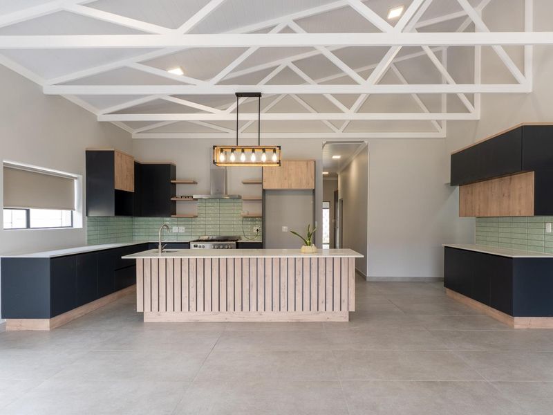 Modern open-plan kitchen featuring exposed white roof trusses, sleek two-tone cabinetry, a central island with stone countertops, and a stylish tiled backsplash.