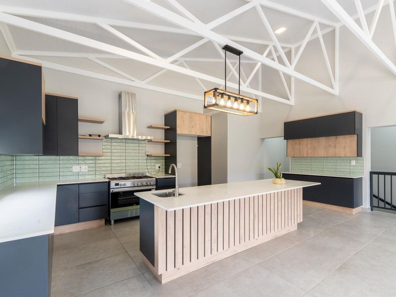 Modern kitchen featuring a large island, stone countertops, two-tone cabinetry, subway tile backsplash, and striking exposed white roof trusses.