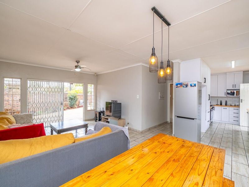 Open-plan living and kitchen area featuring tiled floors, modern pendant lighting, and direct access to the rear patio through a security gate.