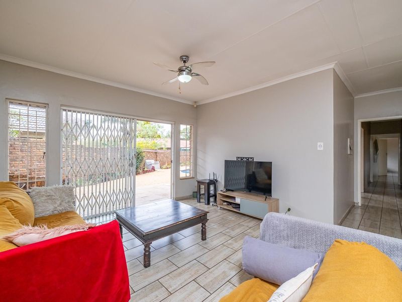 A living room featuring tiled flooring, a ceiling fan, and a sliding glass door with a security gate leading to the outdoor area.