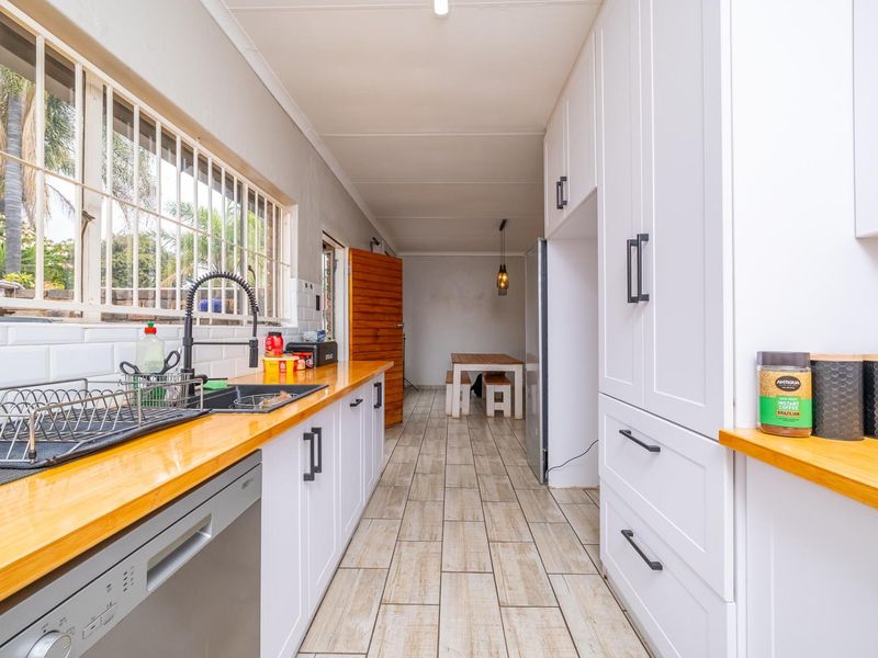 Modern kitchen featuring white cabinetry, warm wooden countertops, subway tile backsplash, and durable ceramic tile flooring with a view to the dining area.