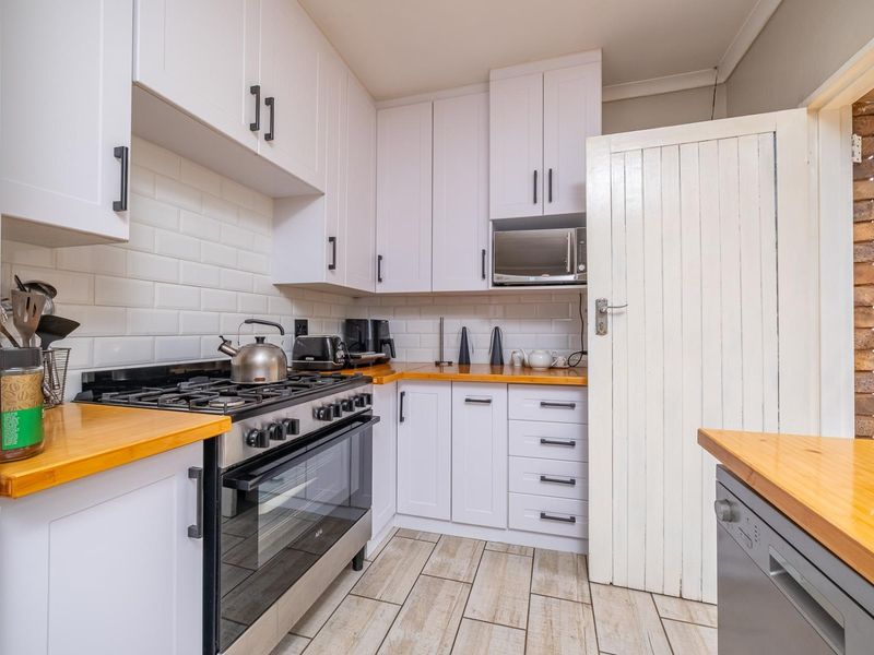 A modern kitchen featuring white cabinetry, wooden countertops, subway tile backsplash, and a gas stove with built-in oven and microwave.