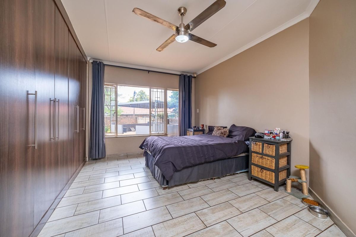 Spacious bedroom featuring large built-in cupboards, tiled flooring, and a ceiling fan, with natural light provided by a large window with security bars.