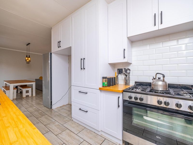 Modern open-plan kitchen featuring white cabinetry, subway tile backsplash, wooden countertops, and a stainless steel gas stove, flowing into the dining area.
