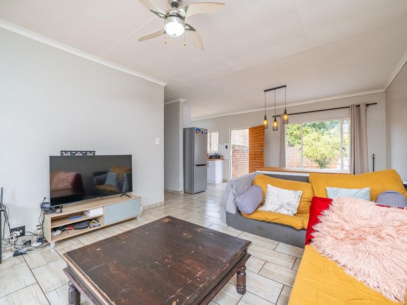 Open-plan living area featuring tiled flooring, a ceiling fan, and a seamless flow into the adjacent kitchen space.